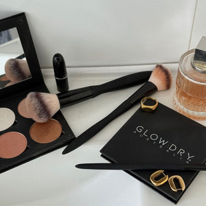Makeup brushes, illuminating palette, lipstick, perfume, and earrings on a white surface with 'GlowDry Australia' branding.