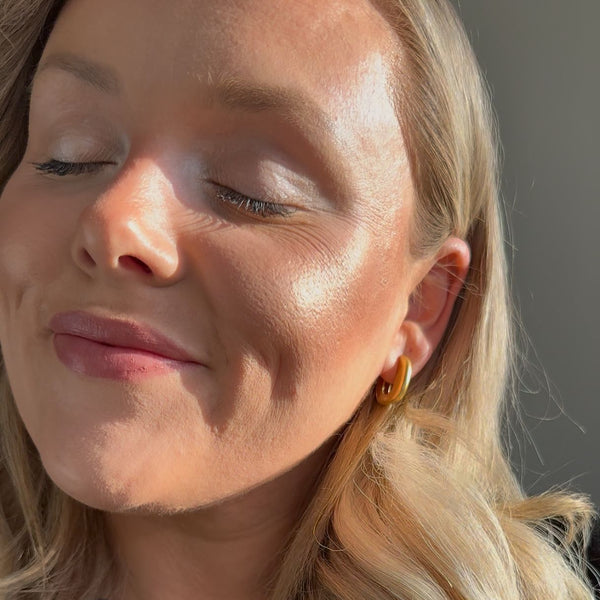 Close-up of a woman with blonde hair and gold earrings against a neutral background showing radiant skin using glowdry illuminating palette