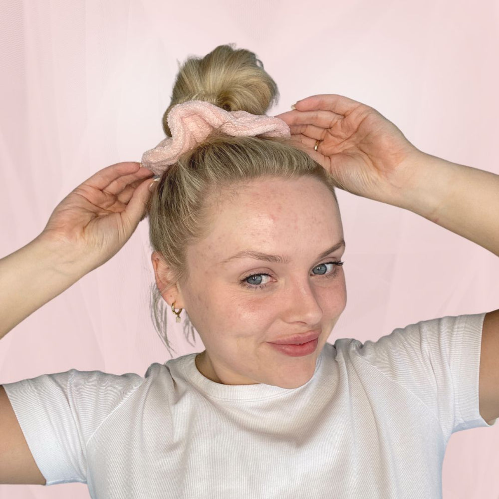 Pink soft terry towel luxe scrunchie in models tan with self tanner and manicured nails to pink backdrop